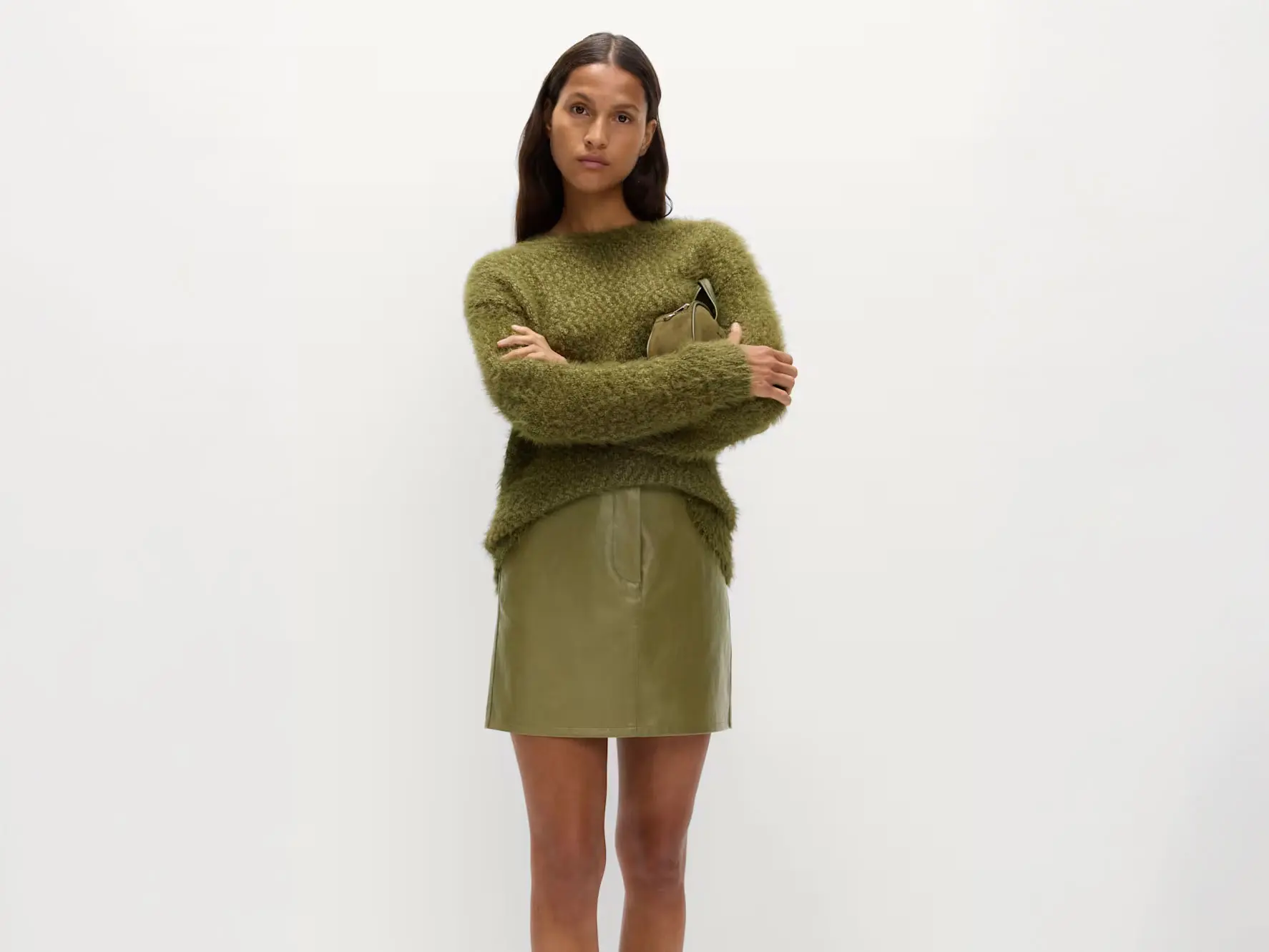 Woman wearing green leather mini skirt with a coordinating jumper and clutch bag