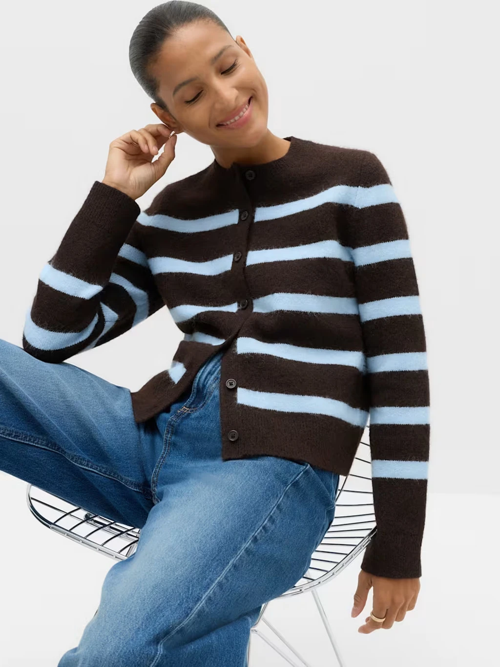Woman wearing a brown and blue striped cardigan and jeans.