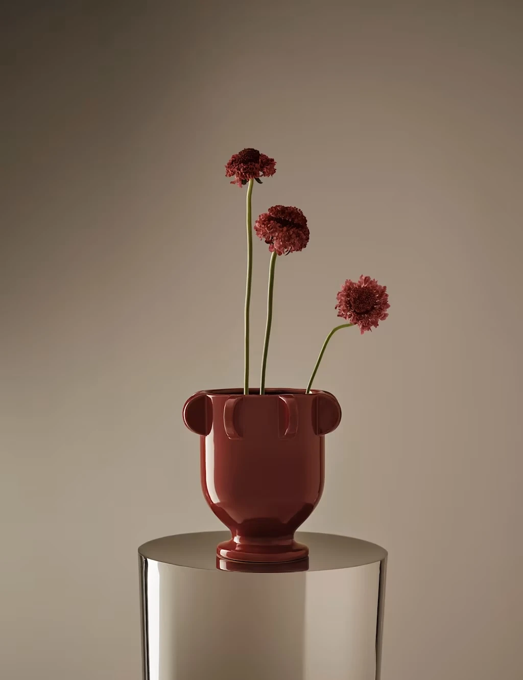 Red glazed vase in a round, footed shape with rounded edging and three red stems.