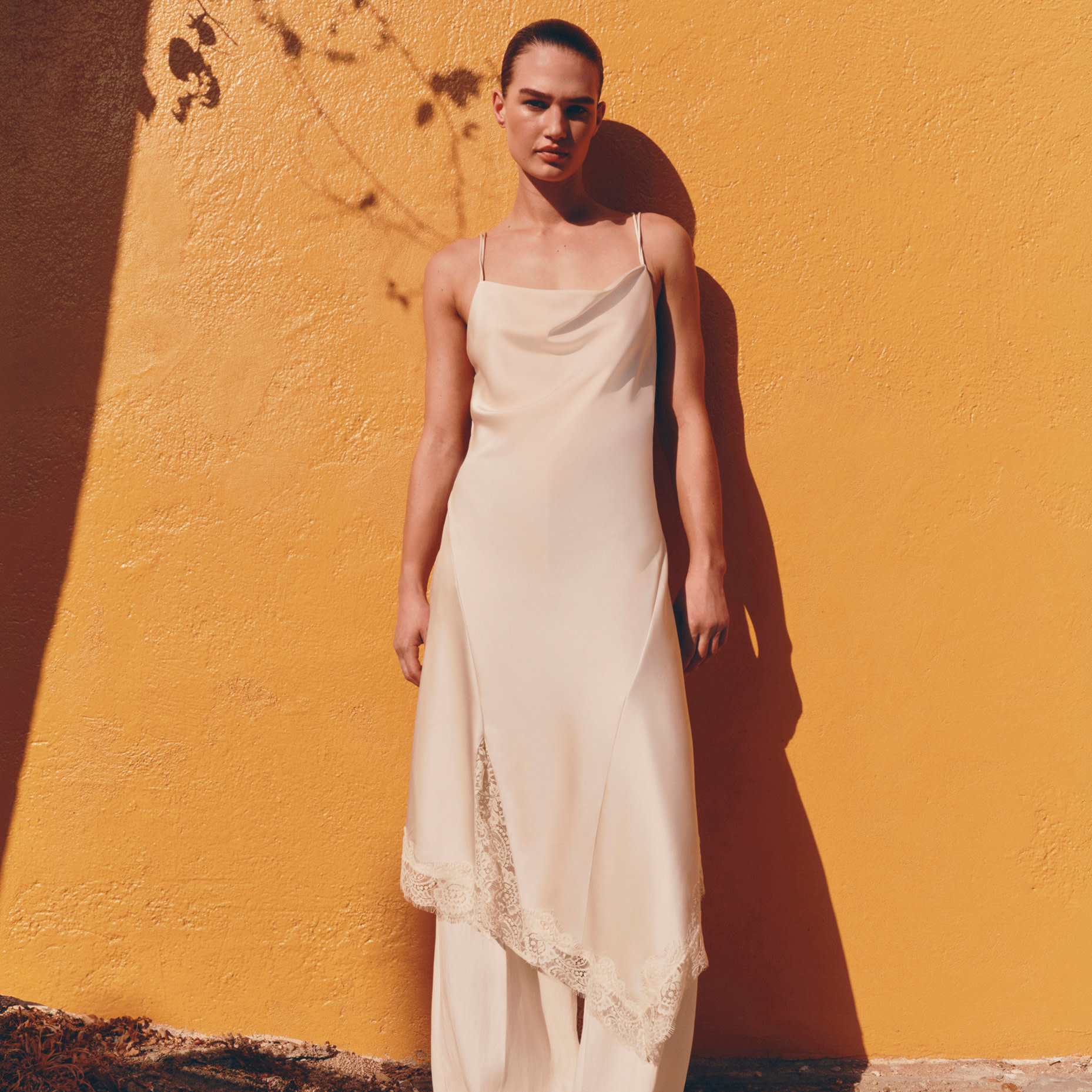 Woman in white dress standing against yellow wall