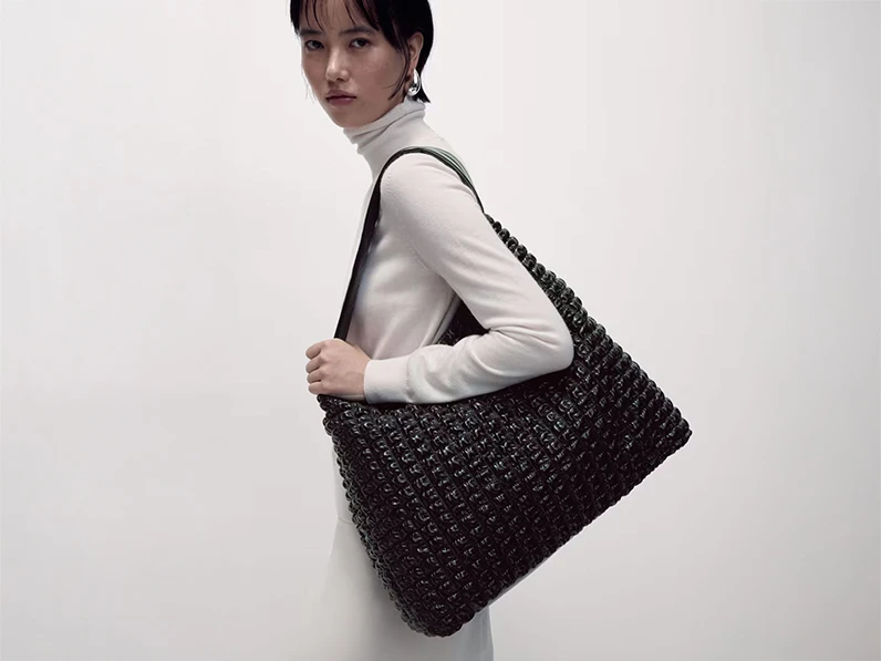 Woman wearing white polo-neck top and a black quilted shoulder bag