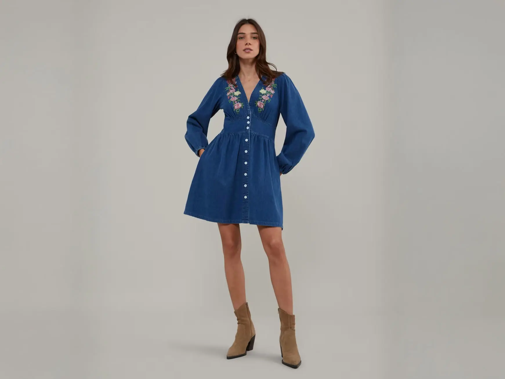 Woman wearing an embroidered denim mini dress with brown suede cowboy boots