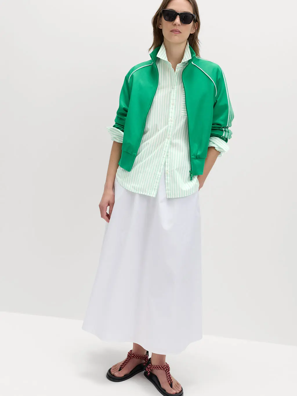 Woman wearing a striped shirt, white maxi skirt, green track jacket and a sandals