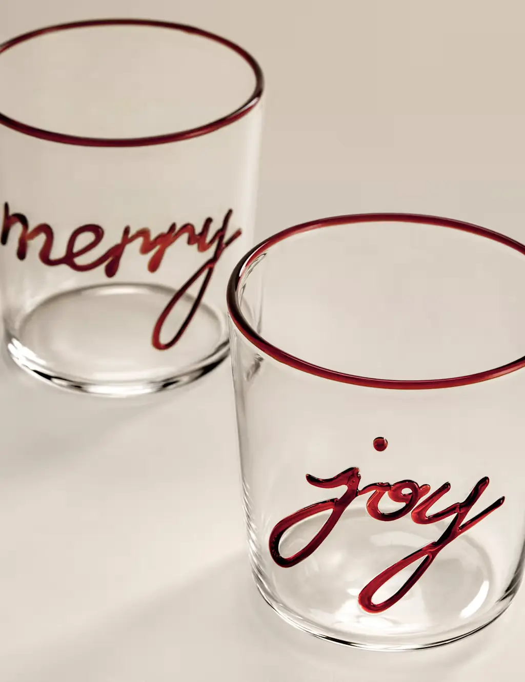 Set of two clear glass tumblers with red text that reads 'merry joy'.