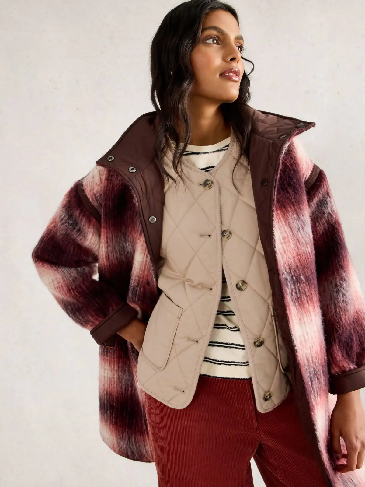Woman wearing checked coat over neutral gilet and striped top 