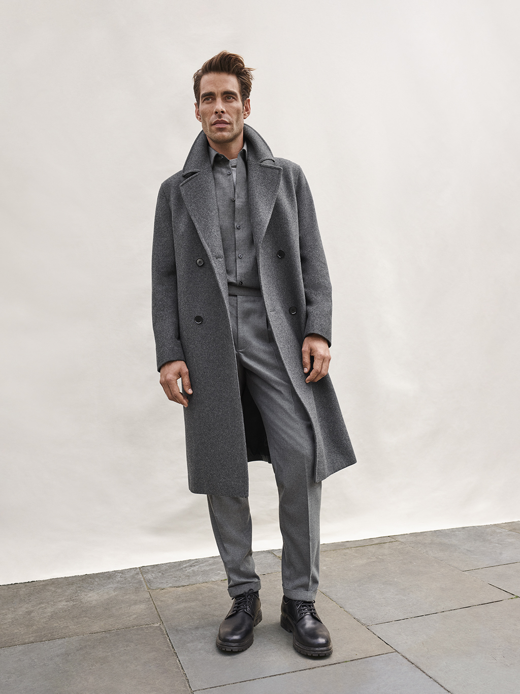 Mad wearing grey tailored coat, grey shirt, grey trousers and black shoes