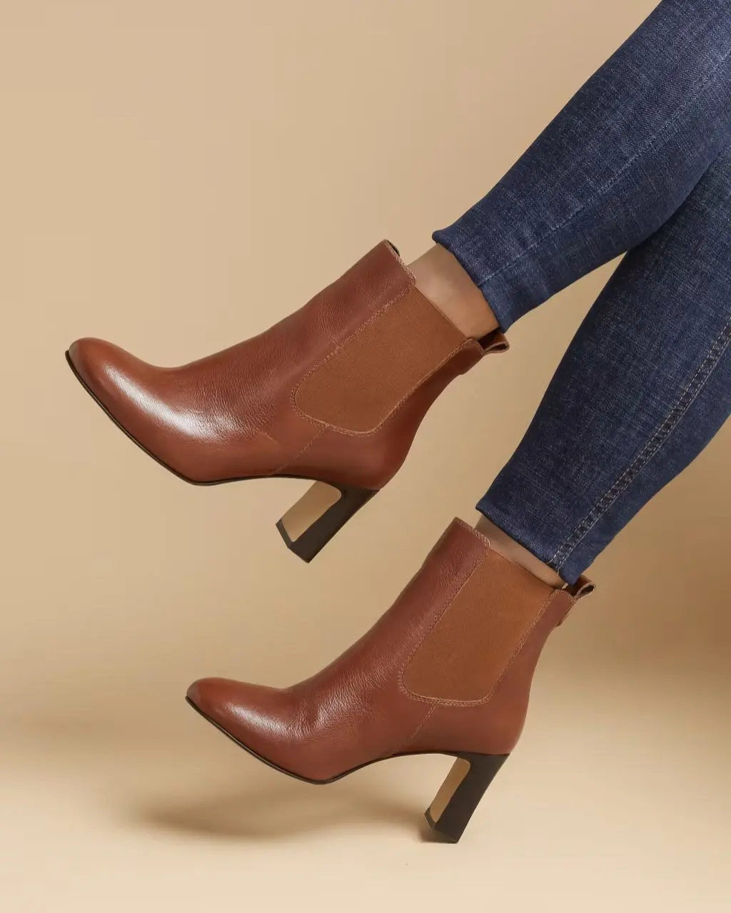 A pair of legs in skinny jeans and brown block heeled high ankle boots