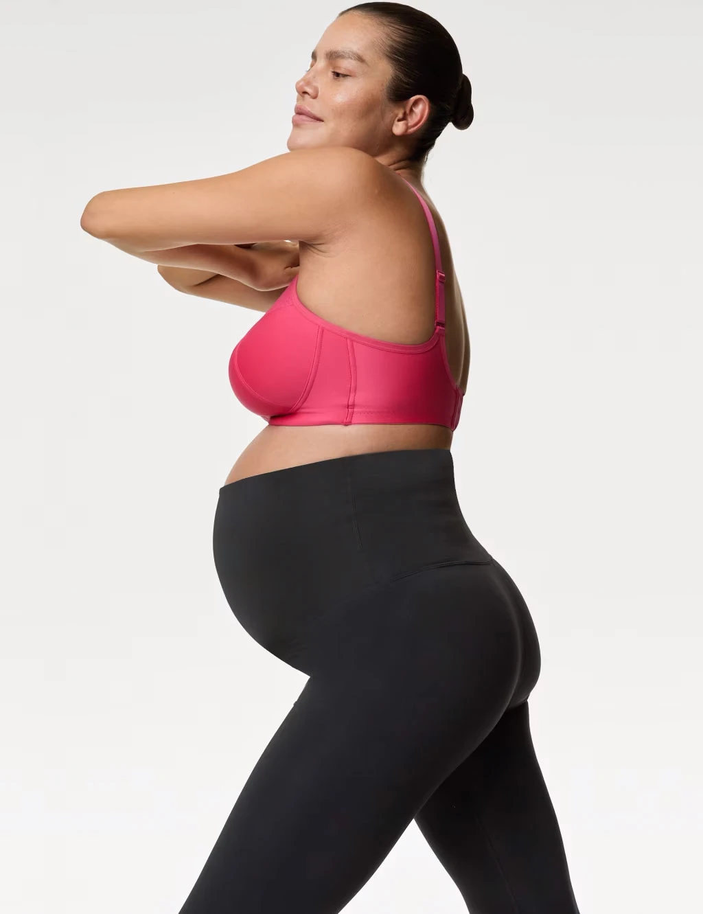 Woman wearing a pink nursing bra with black leggings and silver earrings.