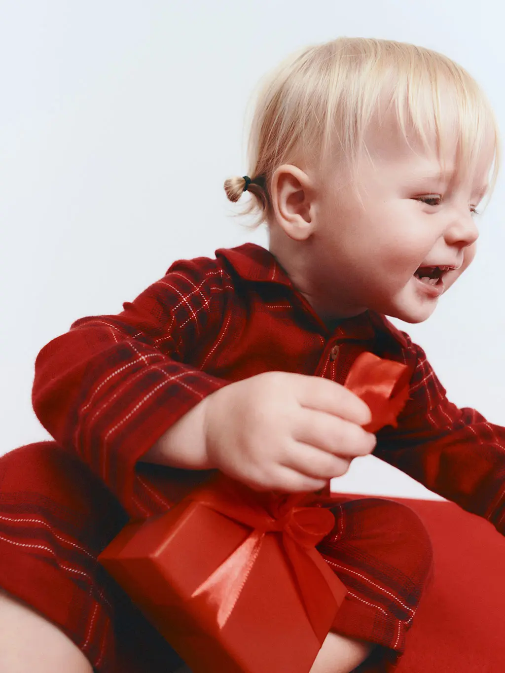 Young girl in a red flannel pyjama set holding a red wrapped present.