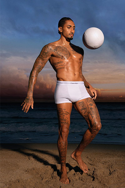 man on beach wearing white boxers kicking a football