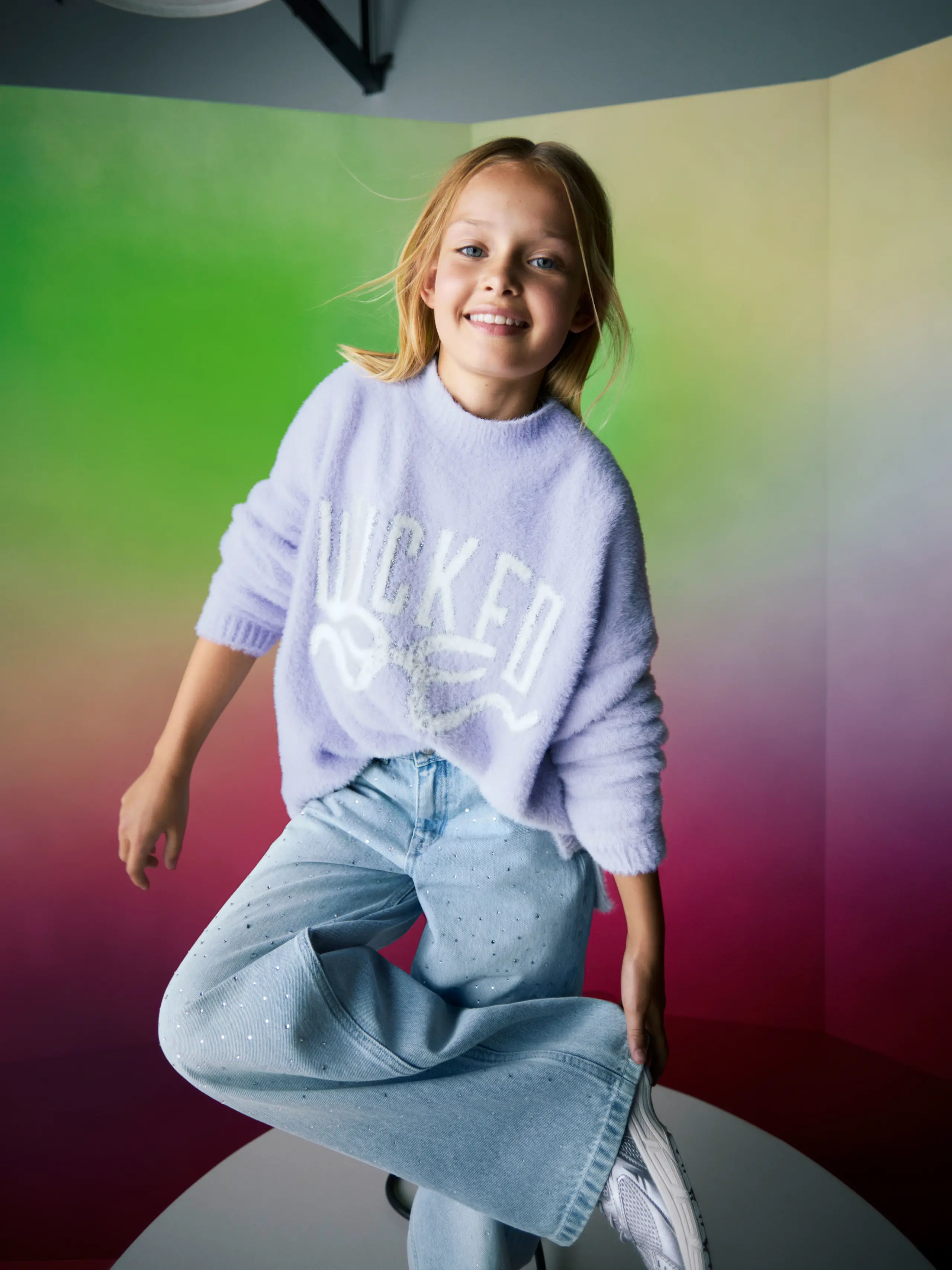 Image of girl wearing Wicked themed lilac jumper and blue jeans