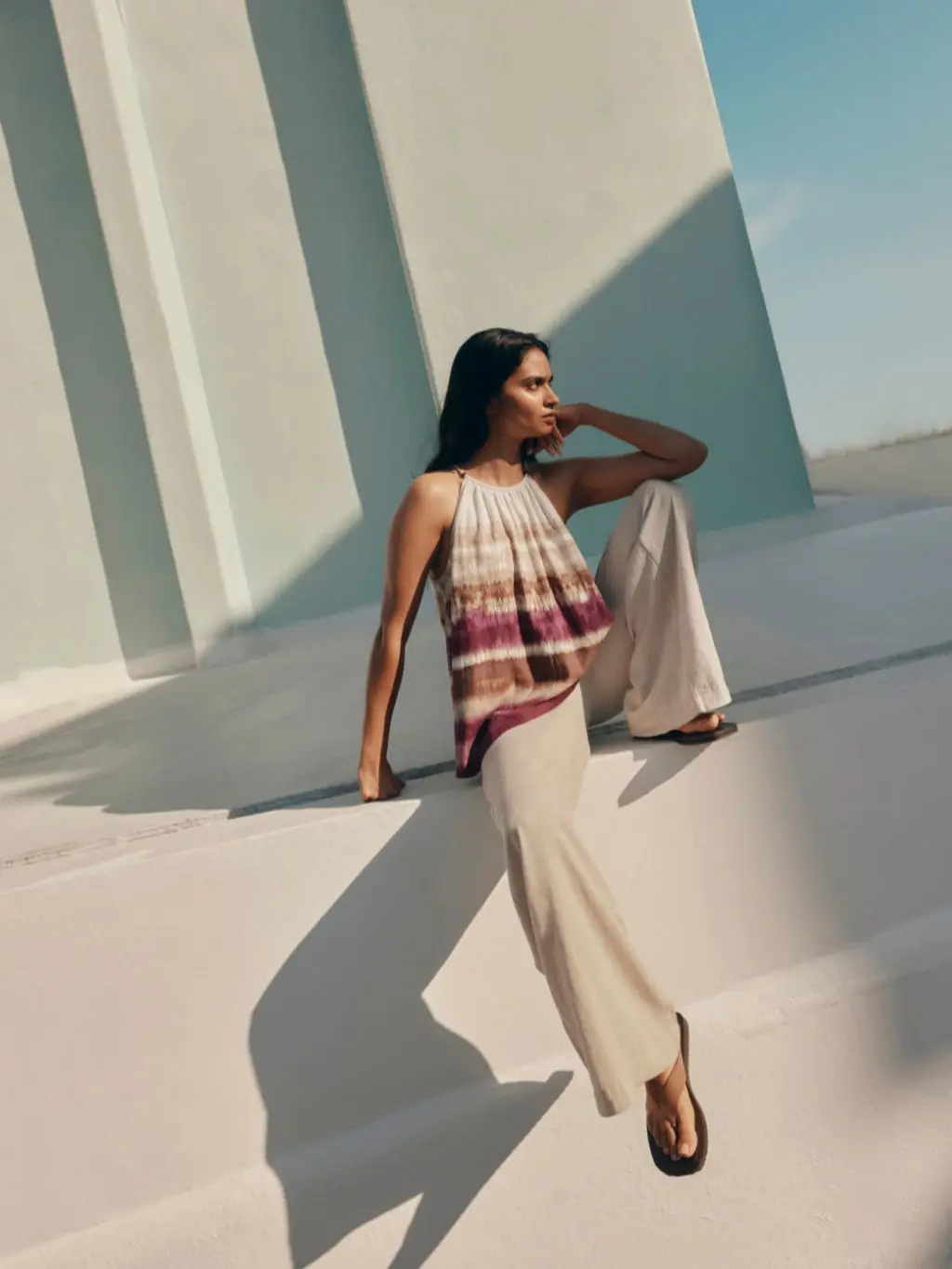 A woman wears wide leg beige linen trousers and a lose ombre halter neck top