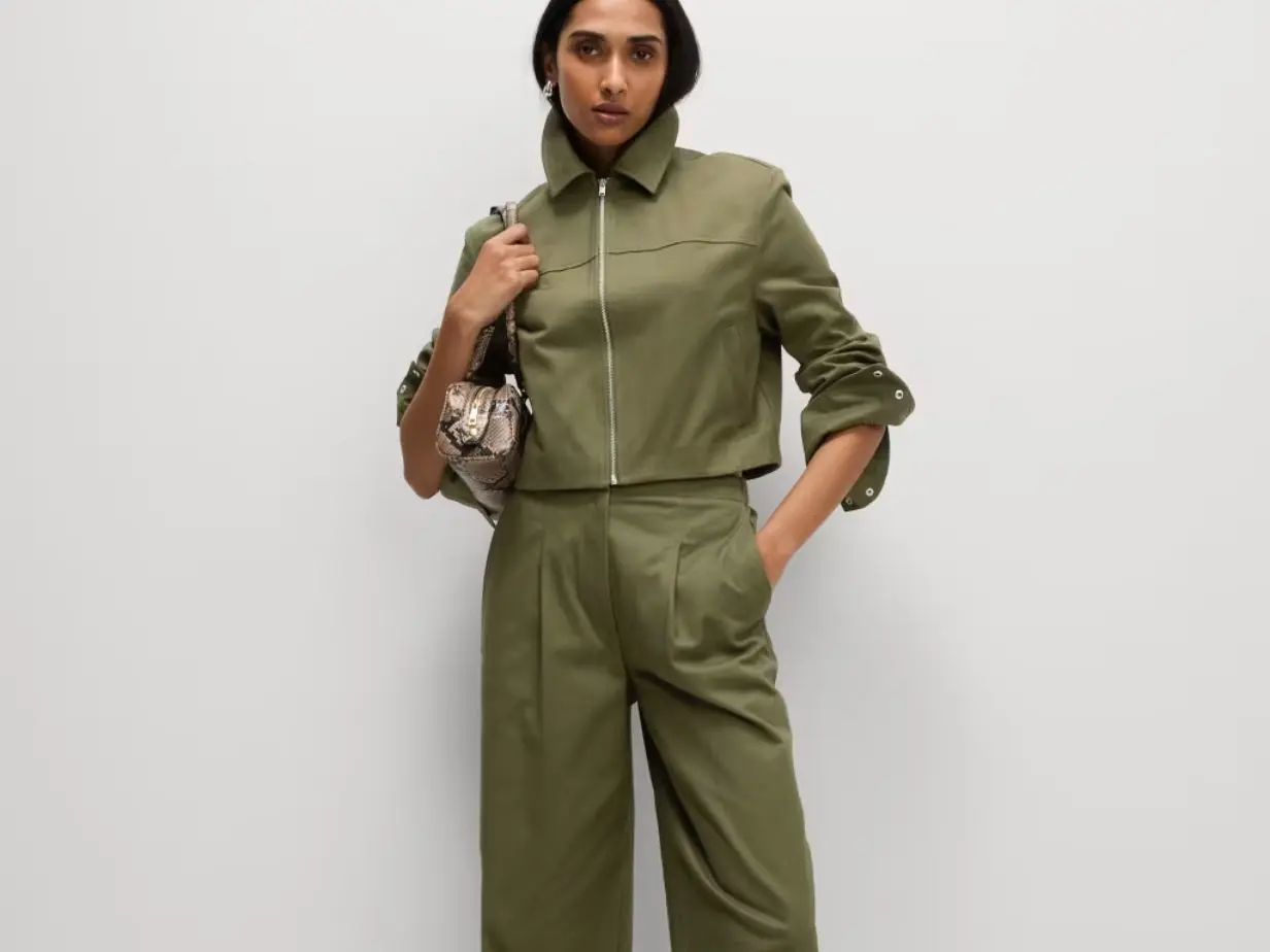 A woman wears a matching green jacket and trousers with a bag over her shoulder