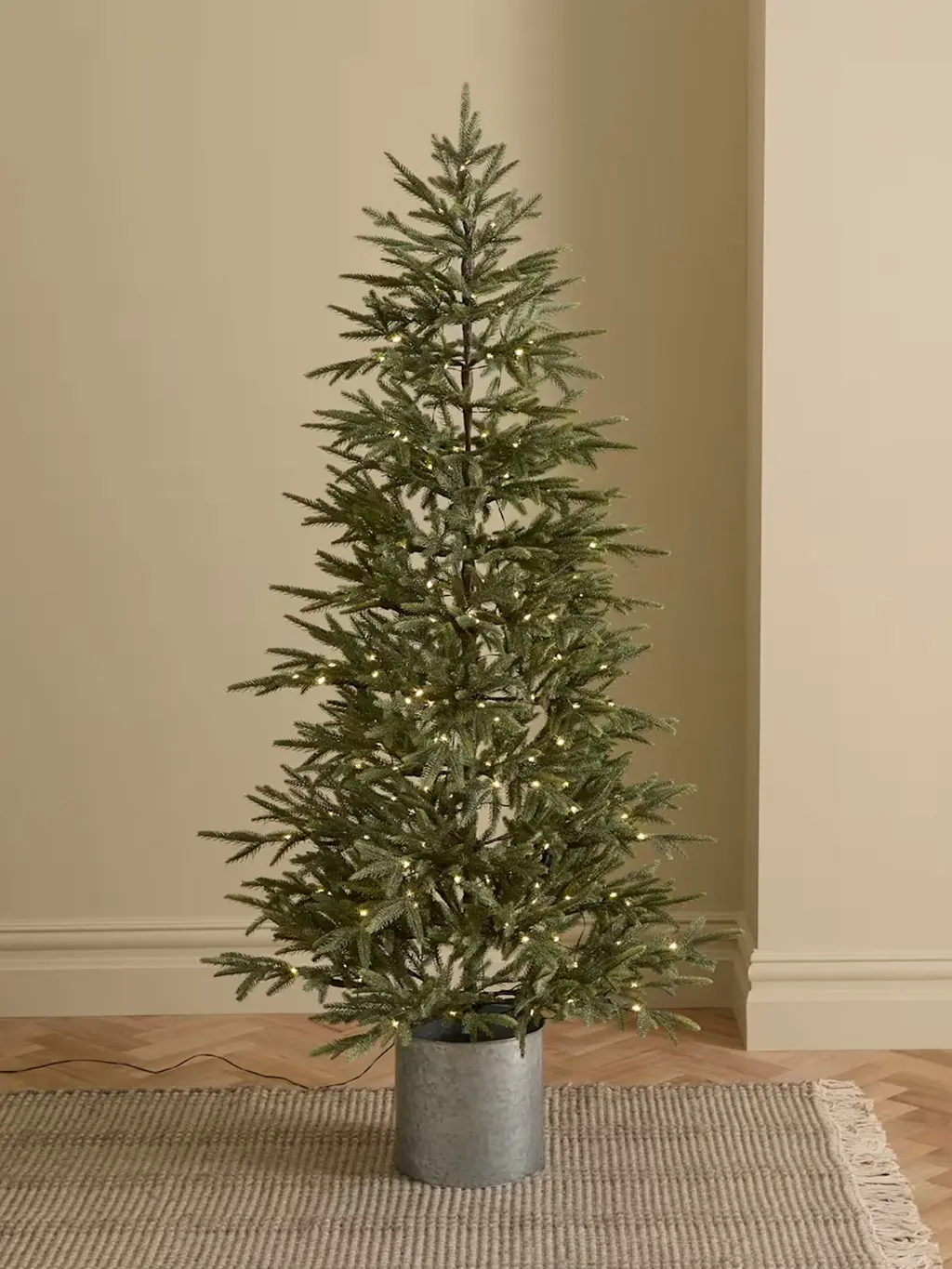 Tall artificial Christmas tree with warm white lights and silver pot.