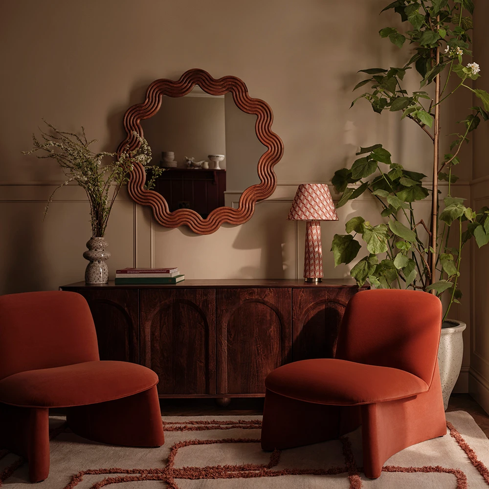 Lounge decorated with velvet chairs, a wavy mirror and a wooden sideboard