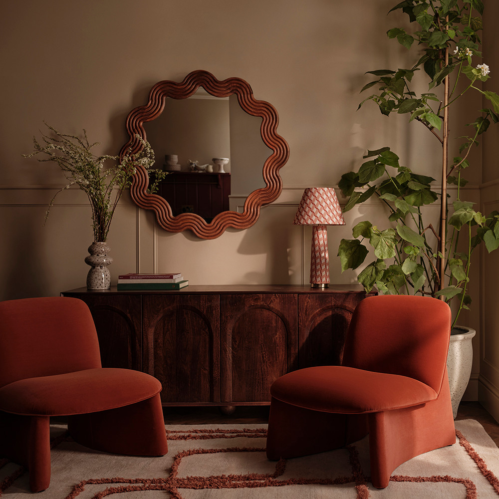 Lounge decorated with velvet chairs, a wavy mirror and a wooden sideboard