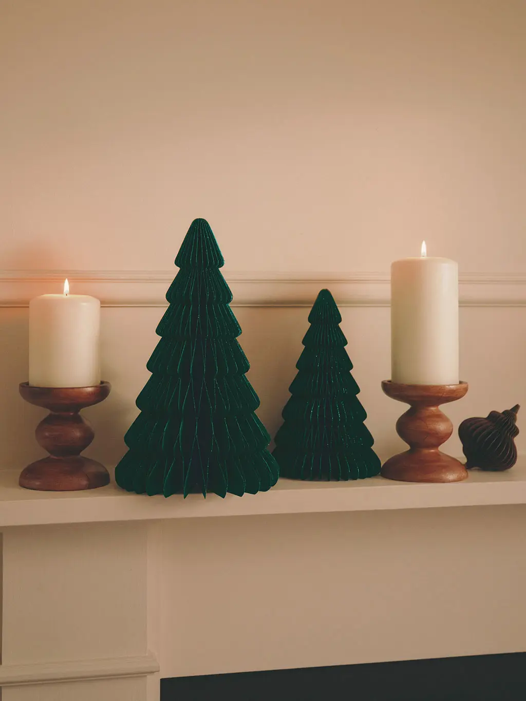 White mantlepiece with green paper tree decorations and wooden pillar candles