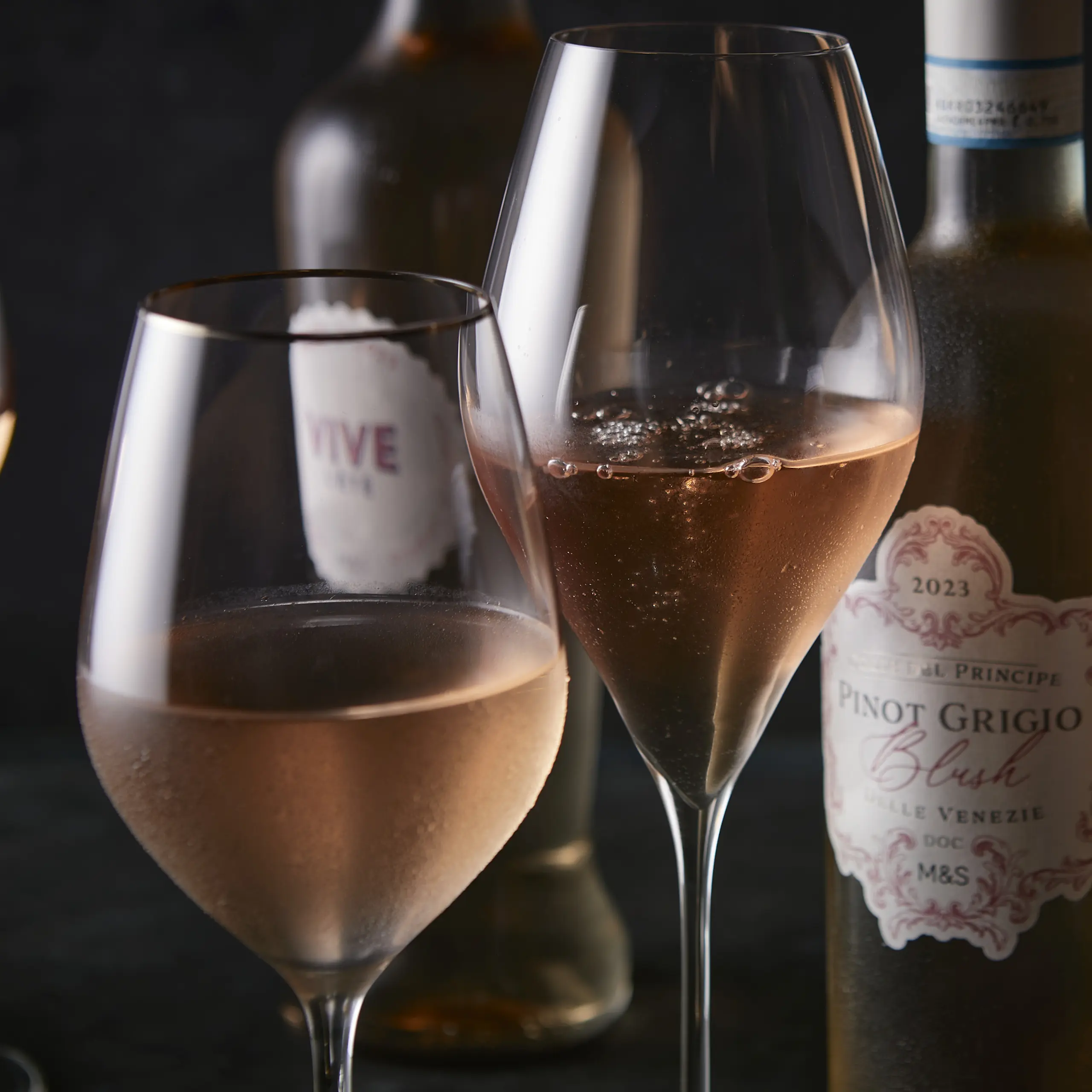 Two glasses of rosé wine with bottles in background
