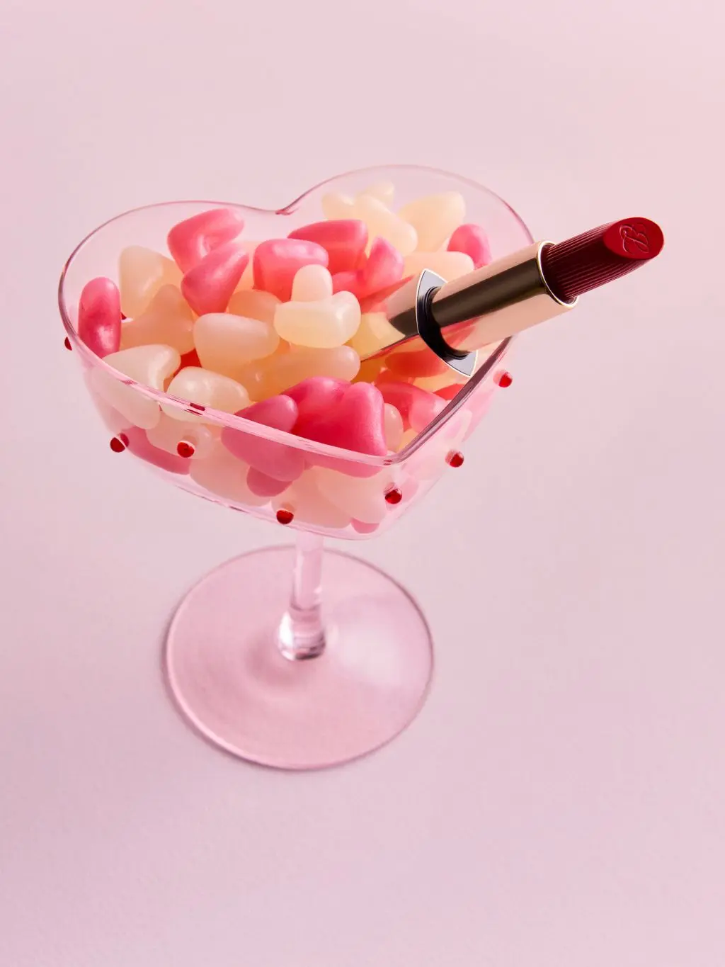 A heart shaped coupe glass filled with jellybeans and a red lipstick