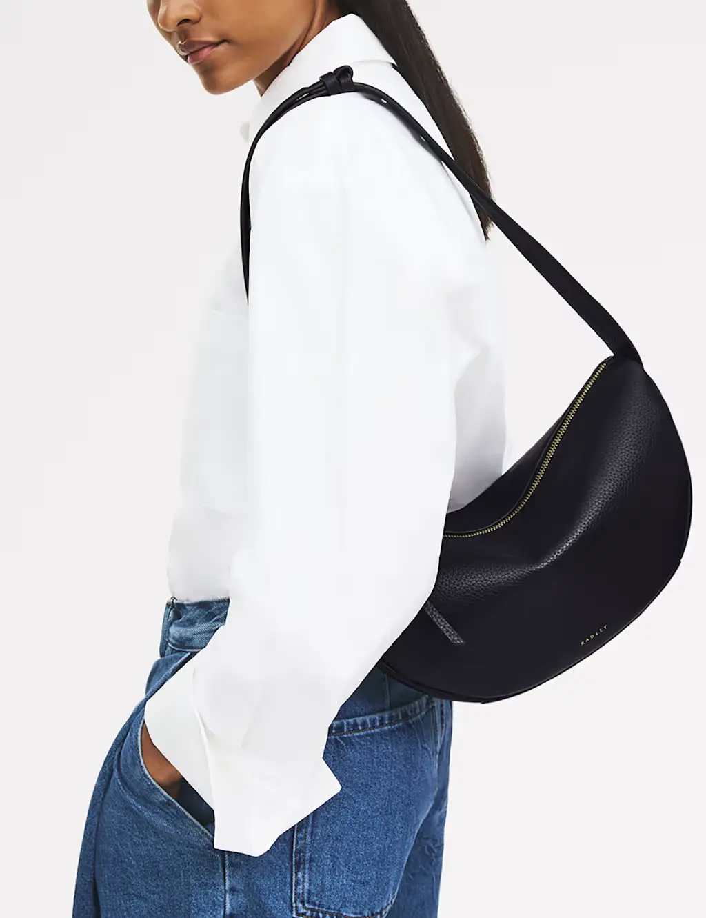 Woman wearing a white T-shirt, blue jeans with a black cross-body bag over her shoulder