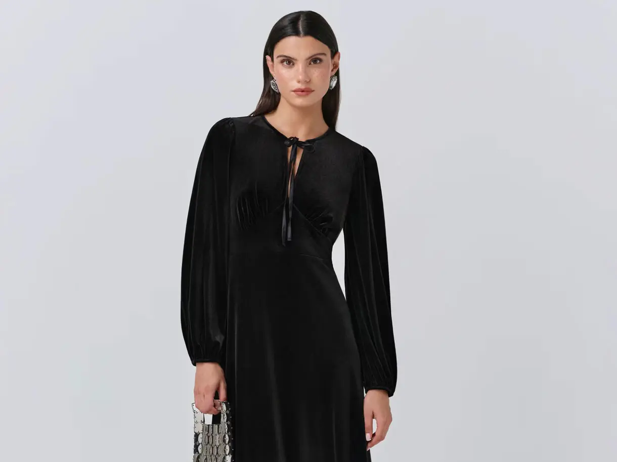 Woman wearing black velvet long-sleeve dress with silver statement earrings and silver metallic bag