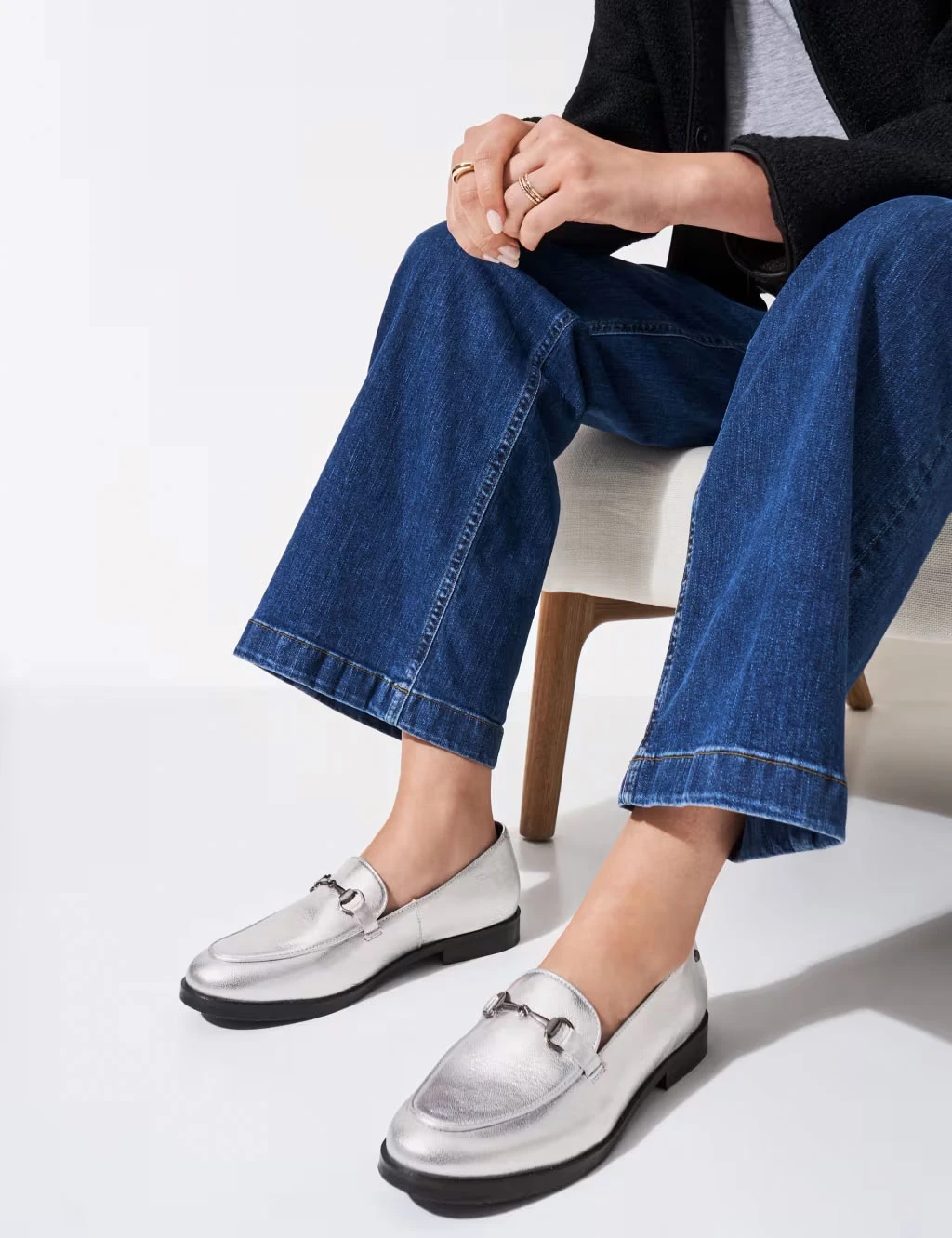 A woman wears blue jeans and silver loafers