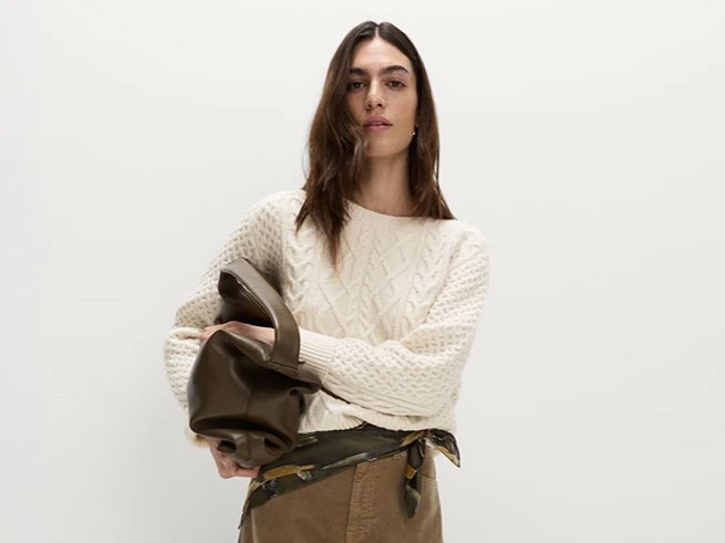 A woman wears a cream cable knit jumper and brown cords
