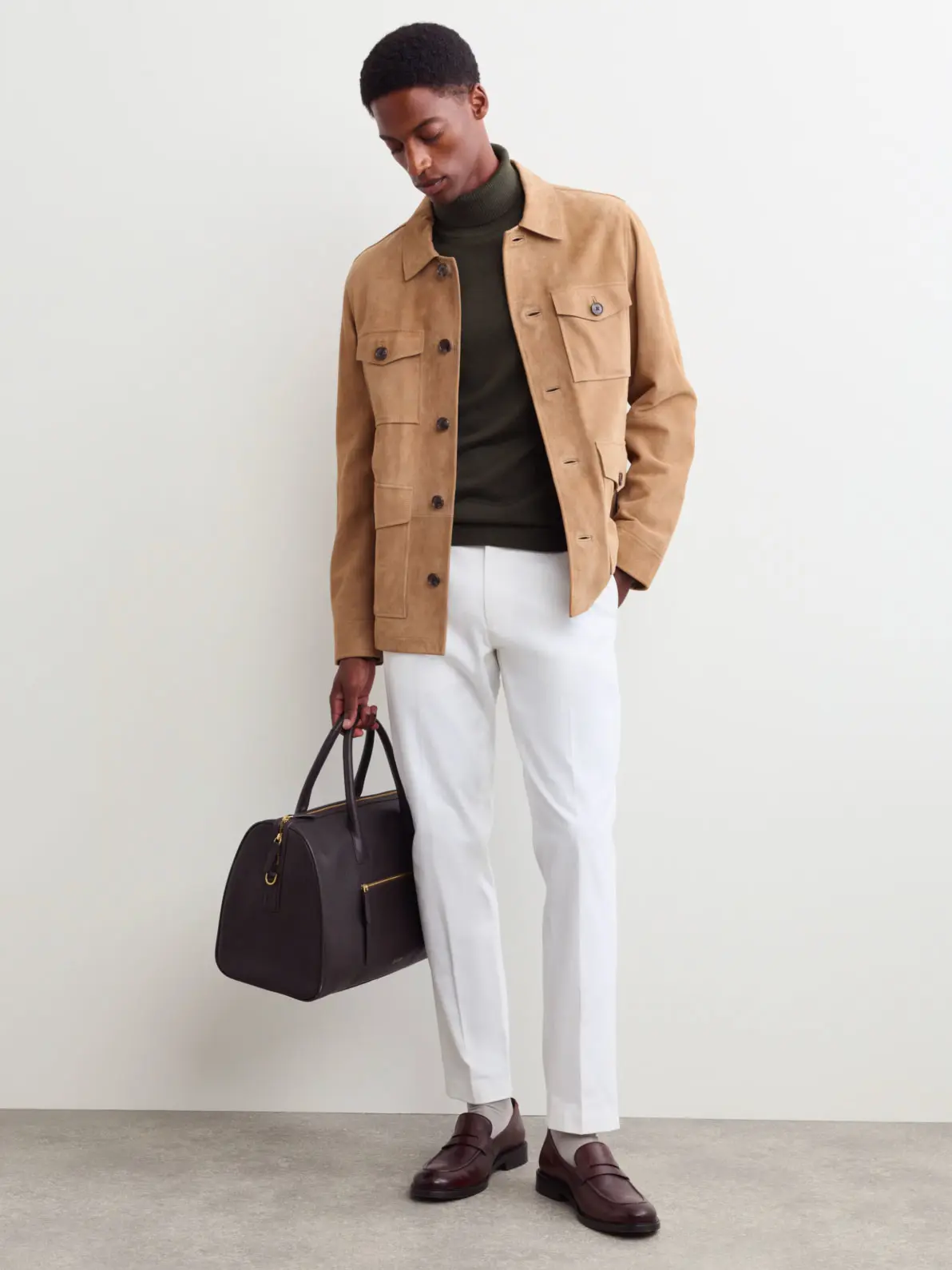 Man wearing neutral jacket, khaki turtle-neck jumper, white trousers and loafers