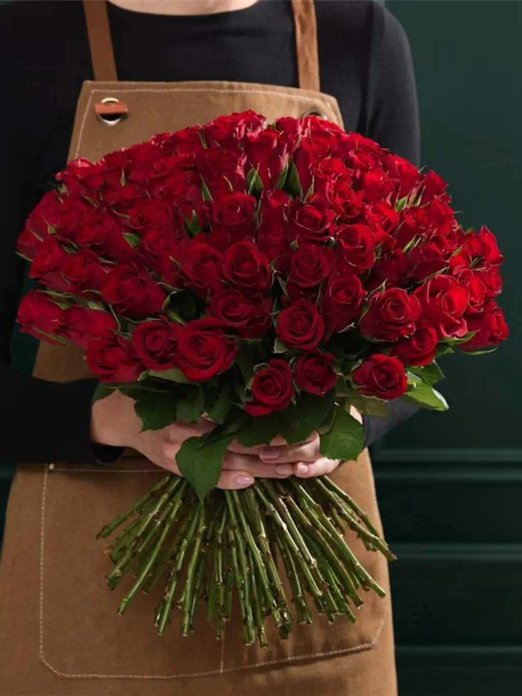 A woman wearing an apron holds a bouquet of 100 red roses