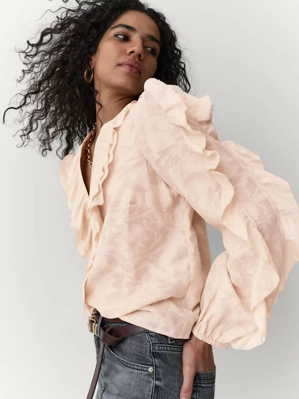 Woman wearing a ruffled blouse with jeans, layered necklaces and brown belt
