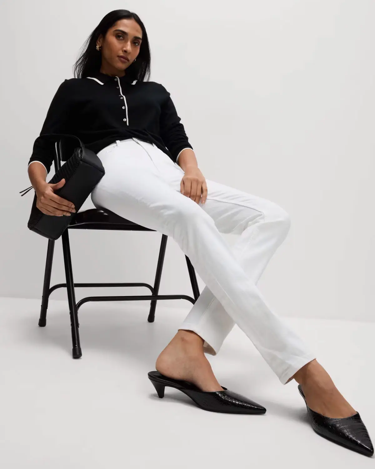 Woman wearing black polo, white jeans and black pointed shoes