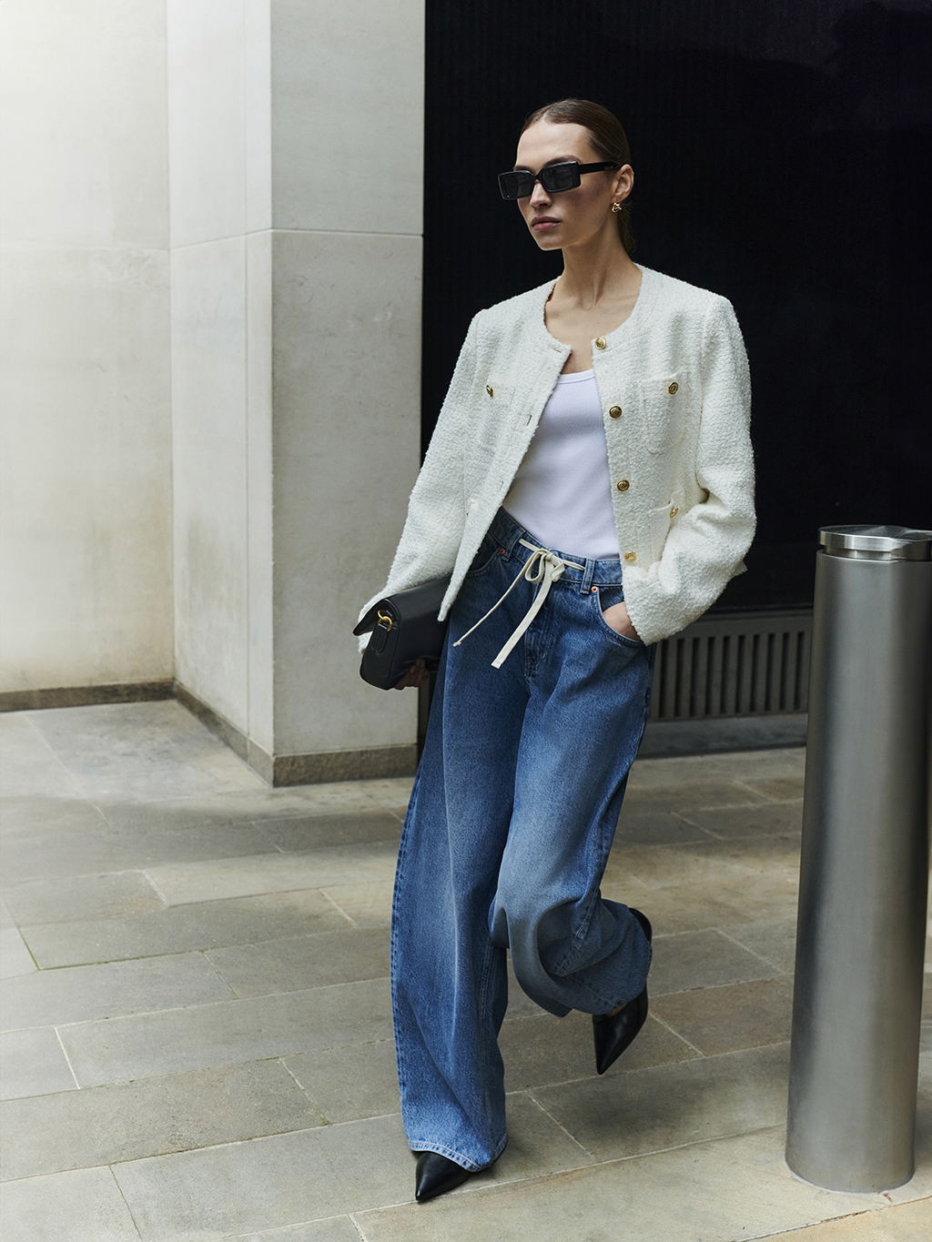 Woman wearing cream collarless jacket, white vest top and blue wide-leg jeans