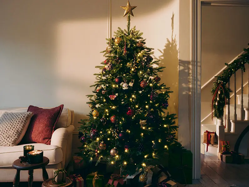 Artificial Christmas tree in a living room decorated with red and gold baubles and star topper.