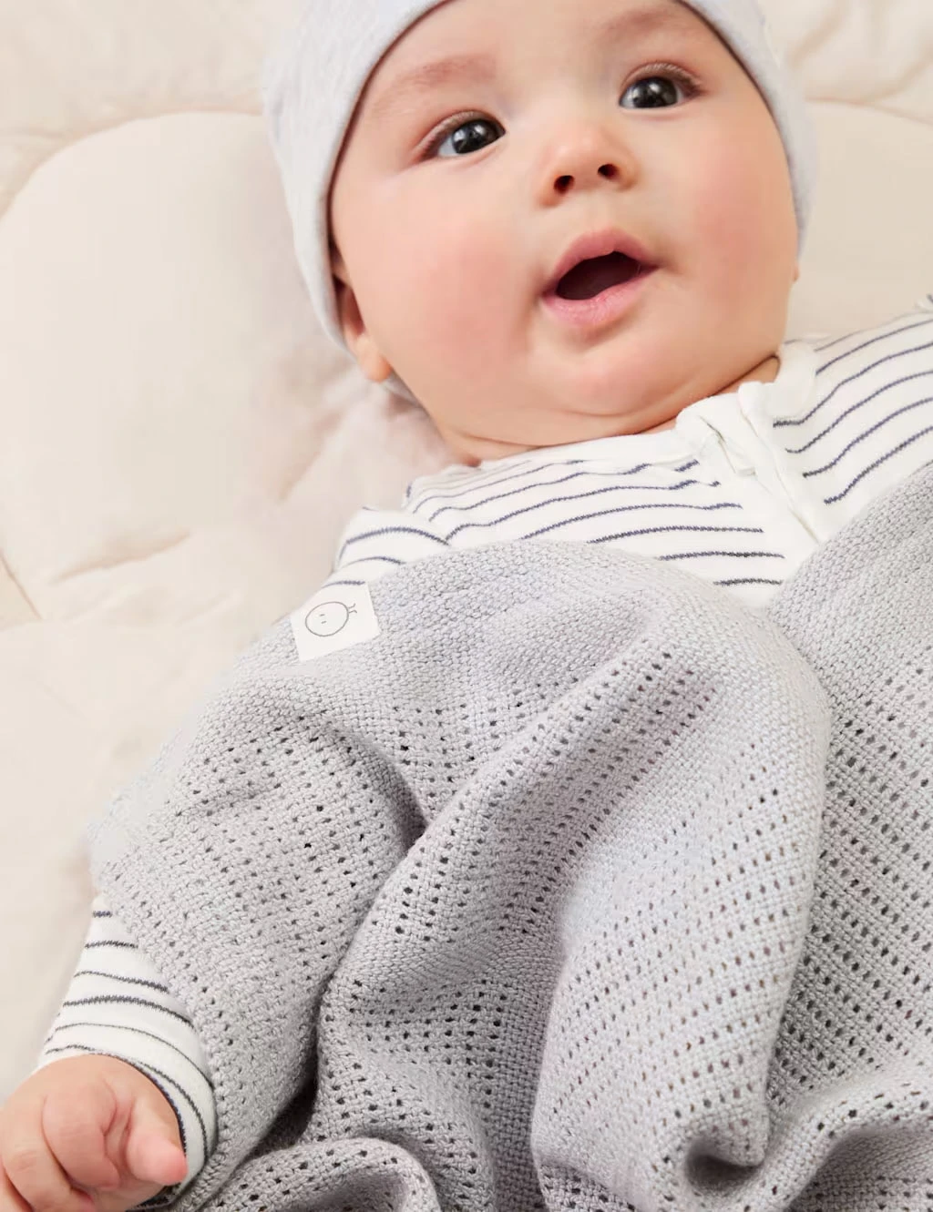 Baby wearing a jersey hat, striped babygrow and grey blanket