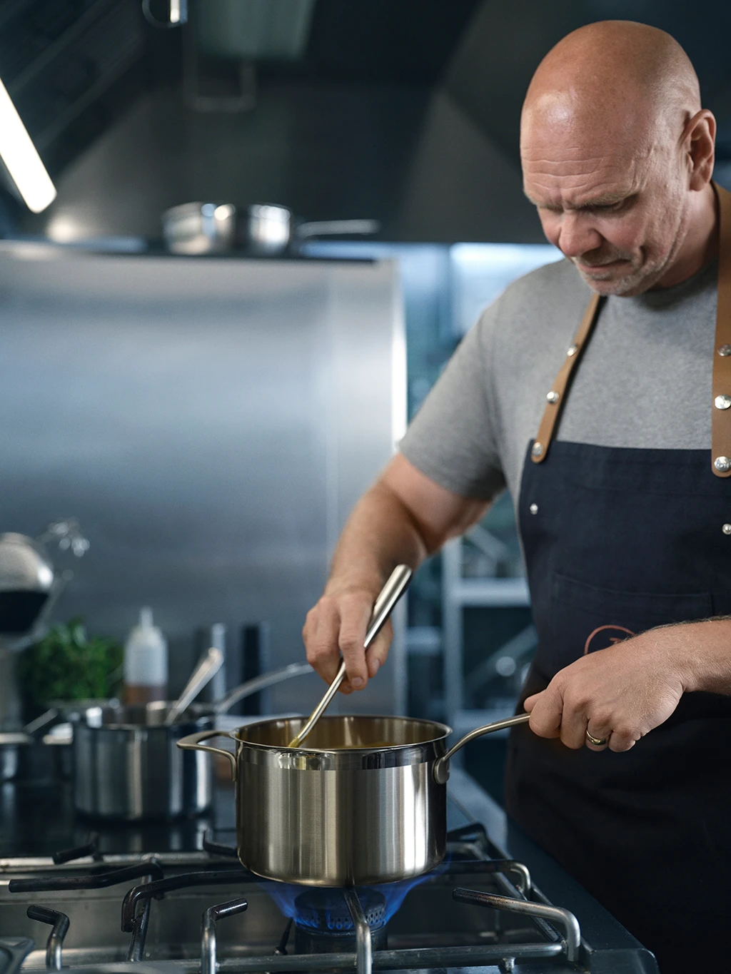 Tom Kerridge cooking wearing a grey T-shirt and navy apron