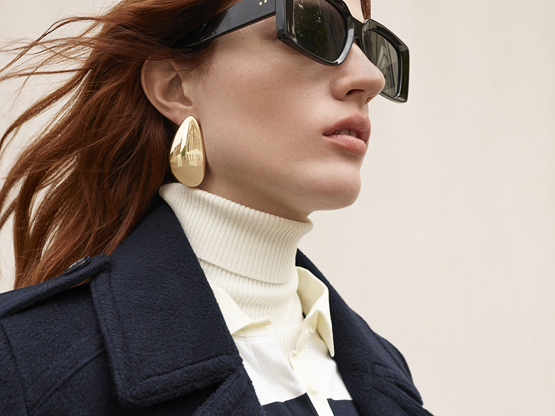 Woman wearing navy wool tailored coat, a polo neck and sunglasses