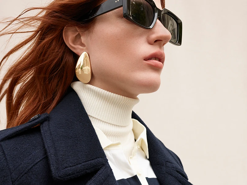 Woman wearing navy wool tailored coat, a polo neck and sunglasses