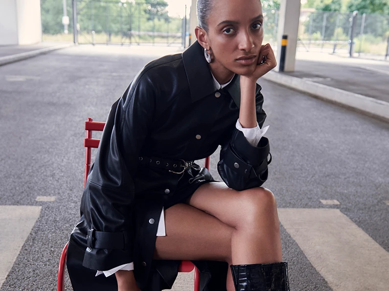 Woman wearing a black belted coat, a white shirt and black knee-high boots