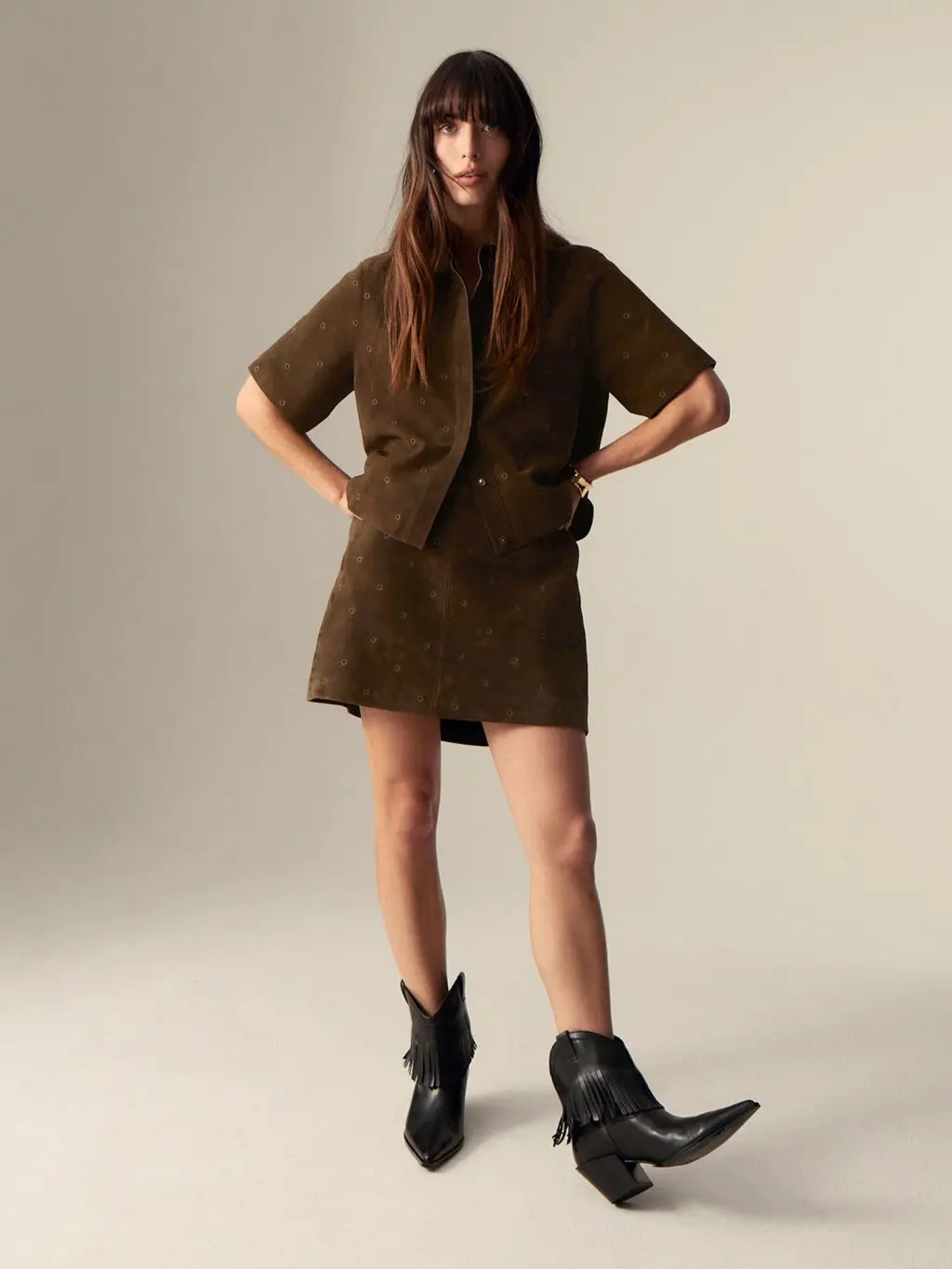A woman wears a matching suede shirt and skirt with western style ankle boots