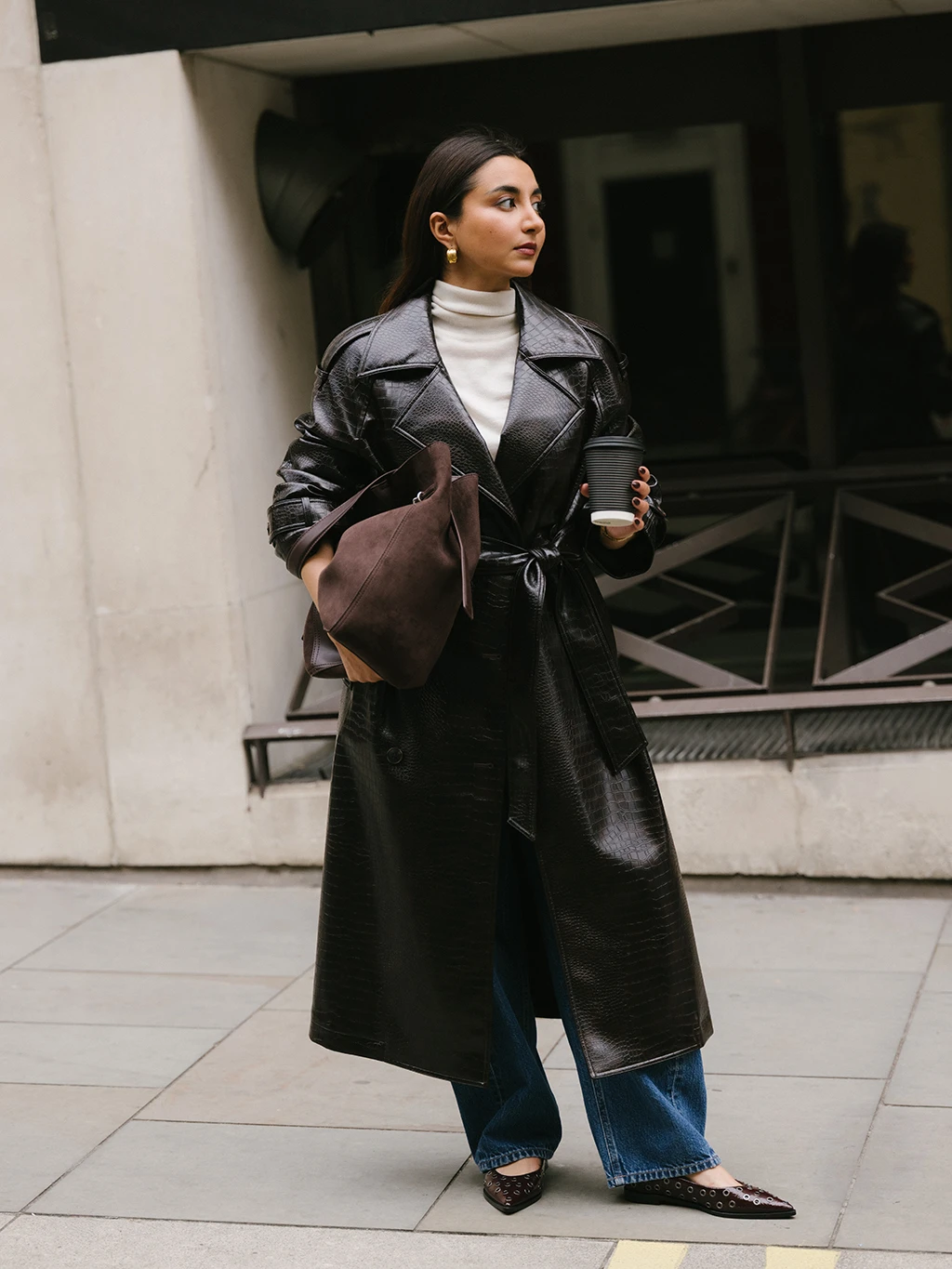 Marina Avraam wearing a dark brown mock-croc trench coat, white polo neck and brown bag