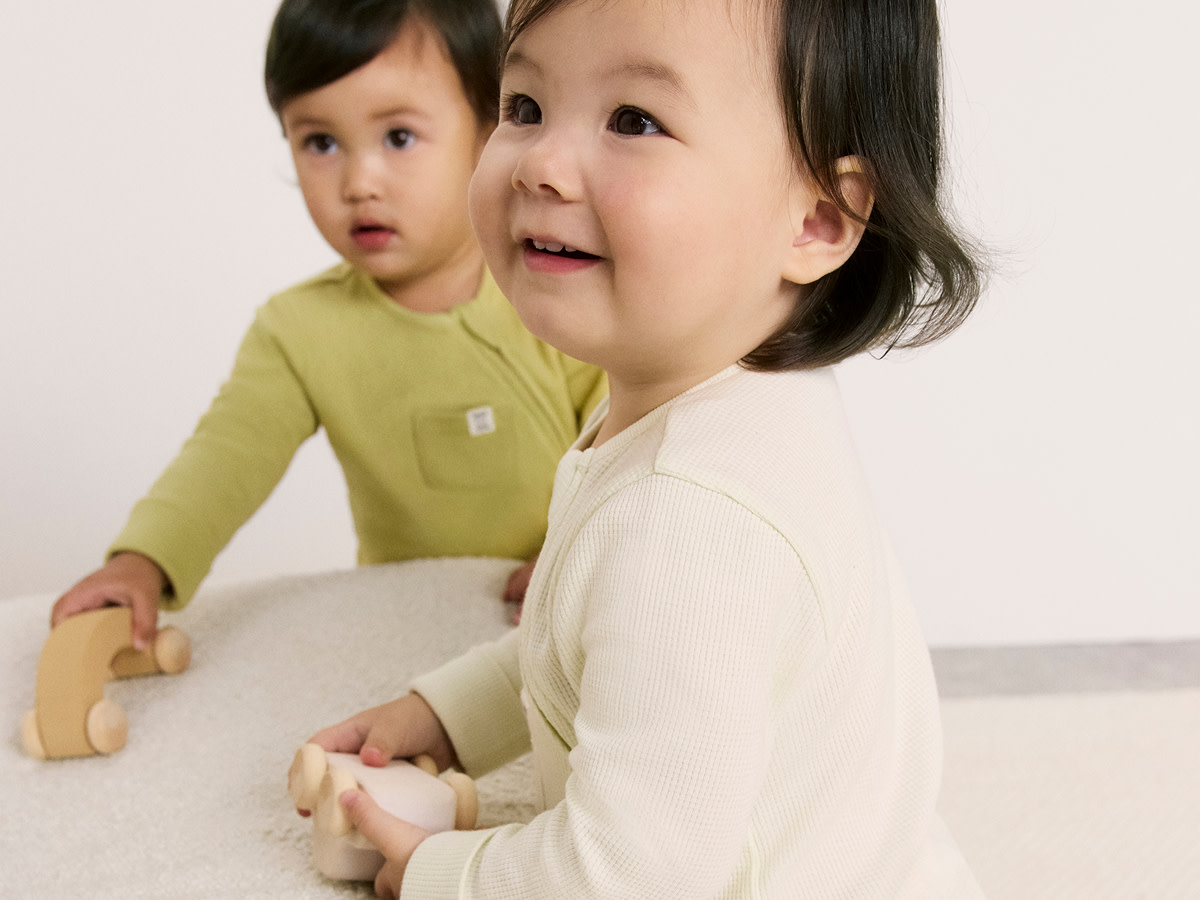 Two babies wearing baby suits playing with wooden toys