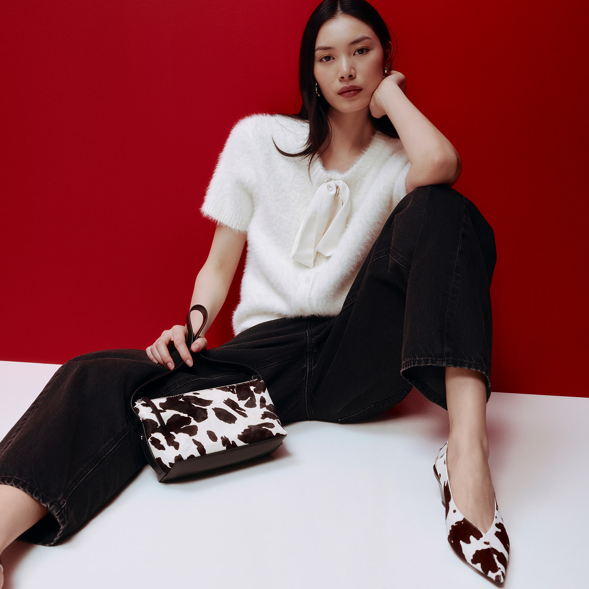 Woman wearing a white bow blouse, black trousers and a cow-print bag and pointed shoes