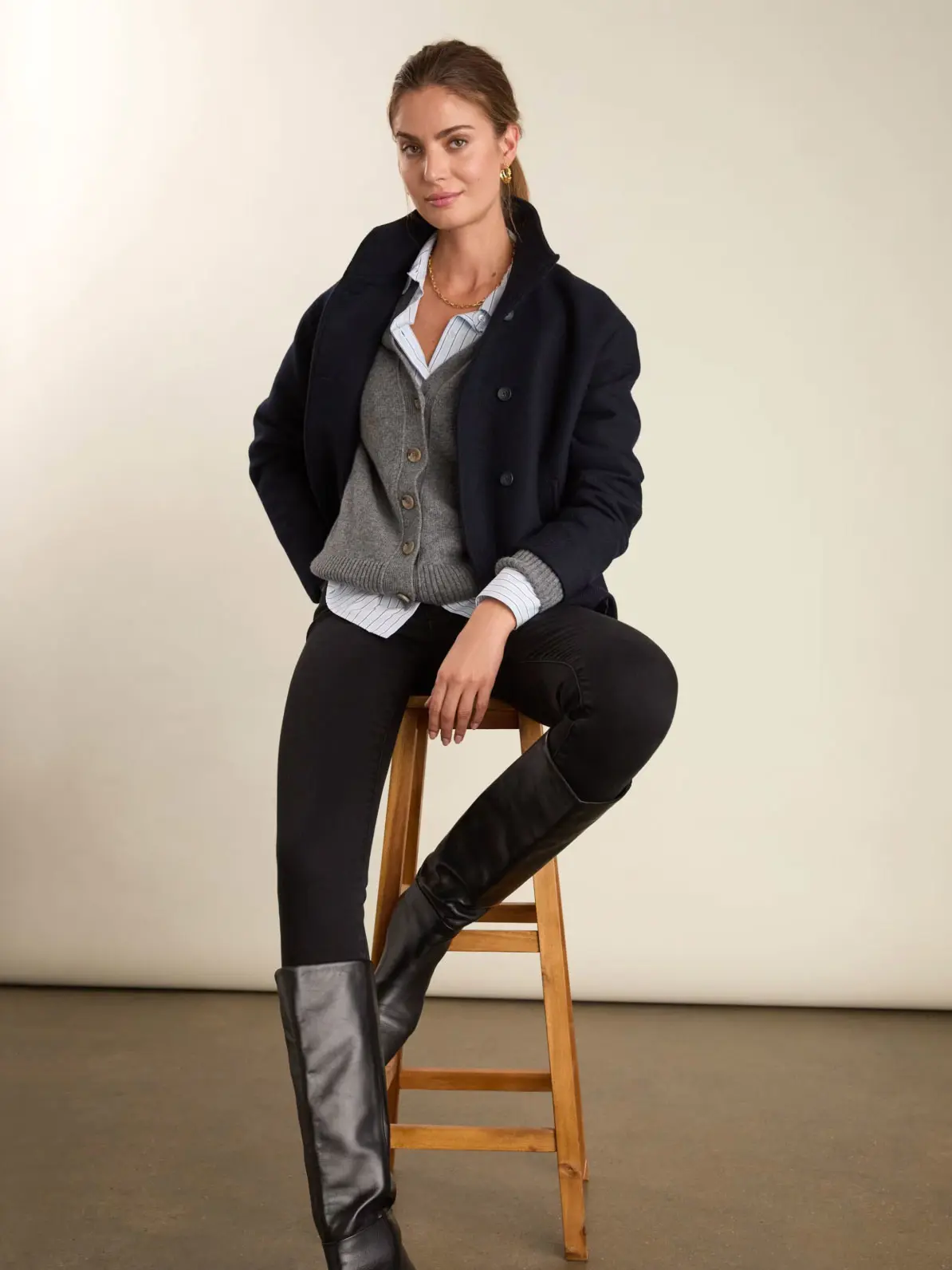 Woman wearing layers over black skinny jeans and black knee-high boots