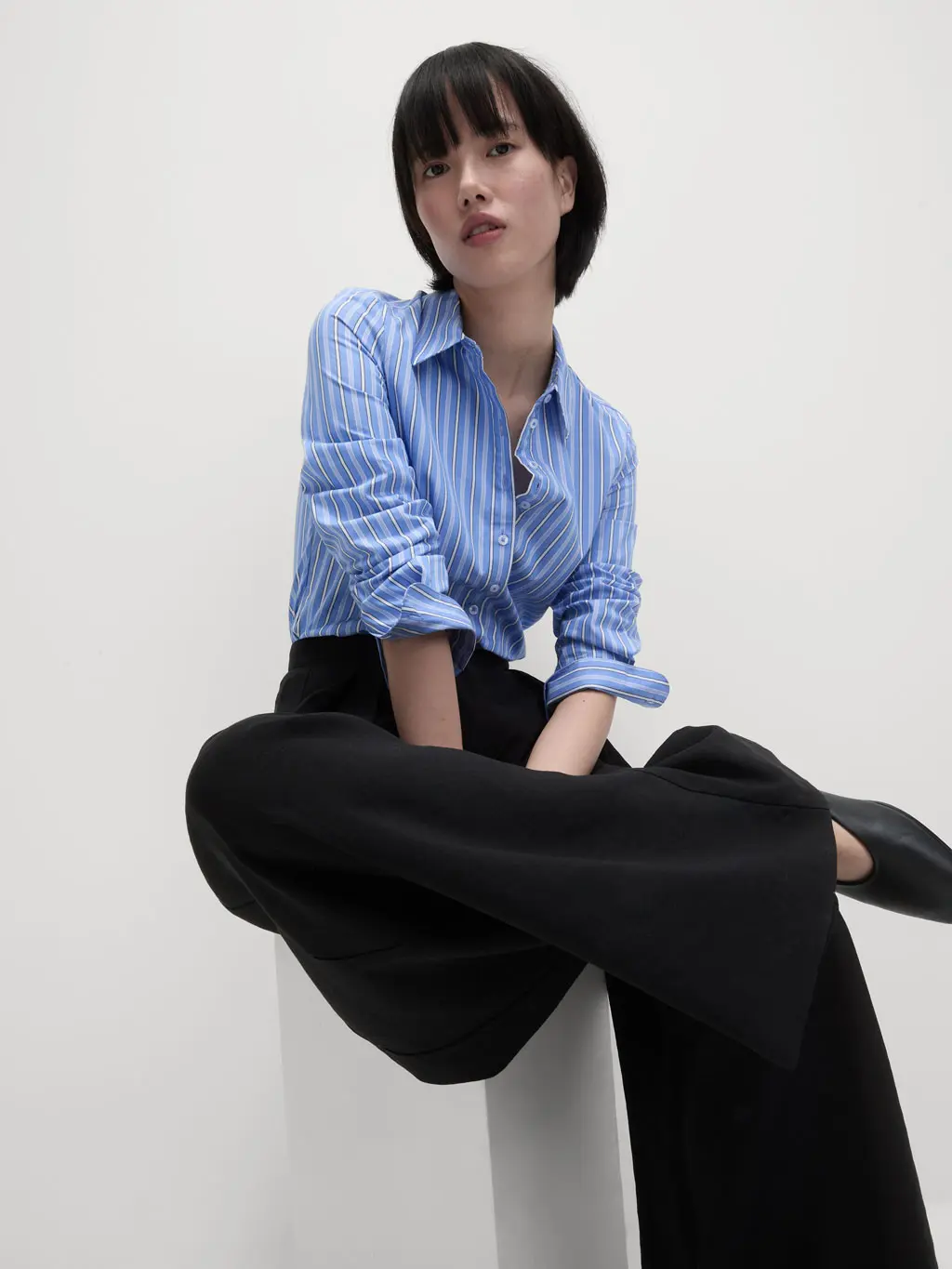 Woman wearing a blue striped shirt with black trousers and black ballet pumps.