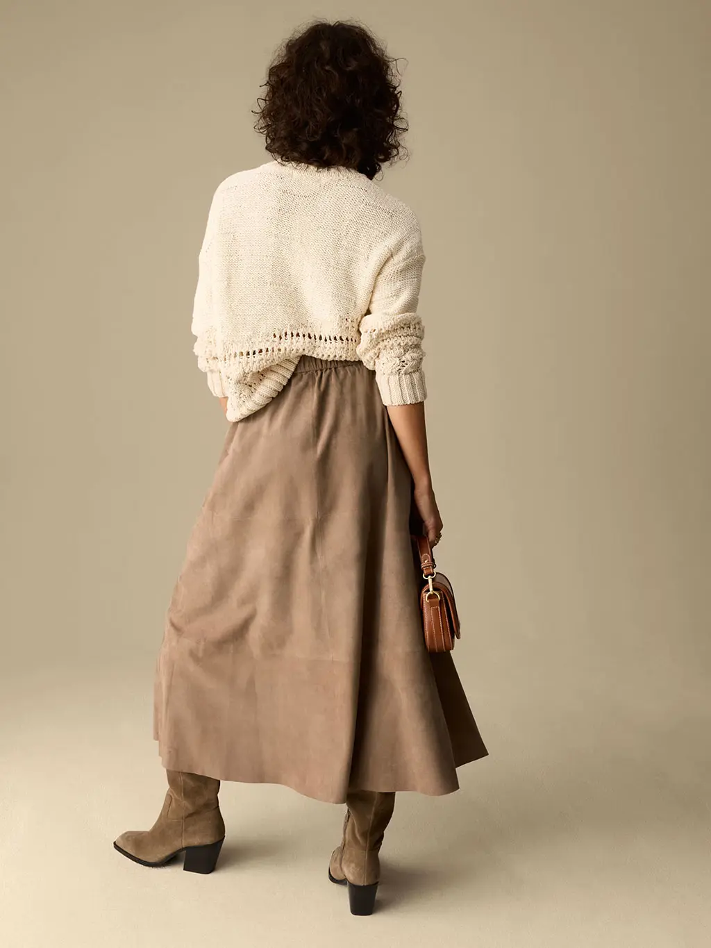 Woman wearing a cream jumper with a suede skirt and cowboy boots
