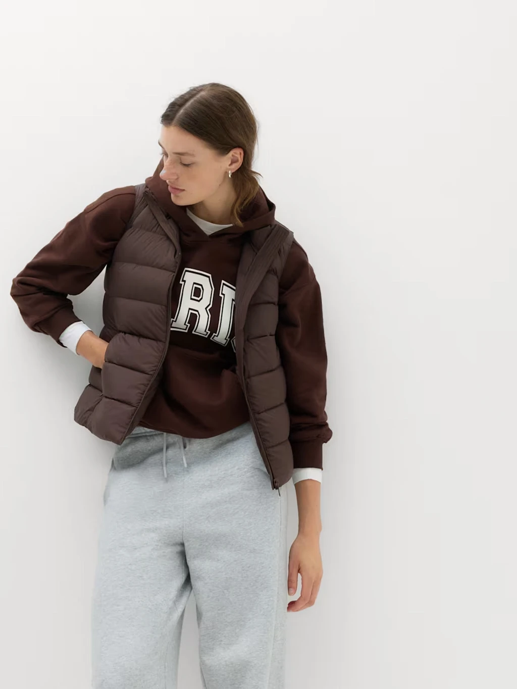 Woman in grey joggers, brown hoodie and padded brown gilet.