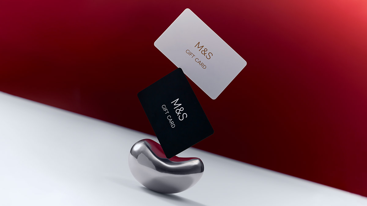 M&S gift cards balancing on a silver pebble against a red background