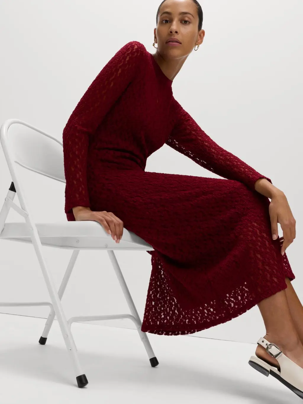 A woman sits on a white chair wearing a long burgundy knitted dress