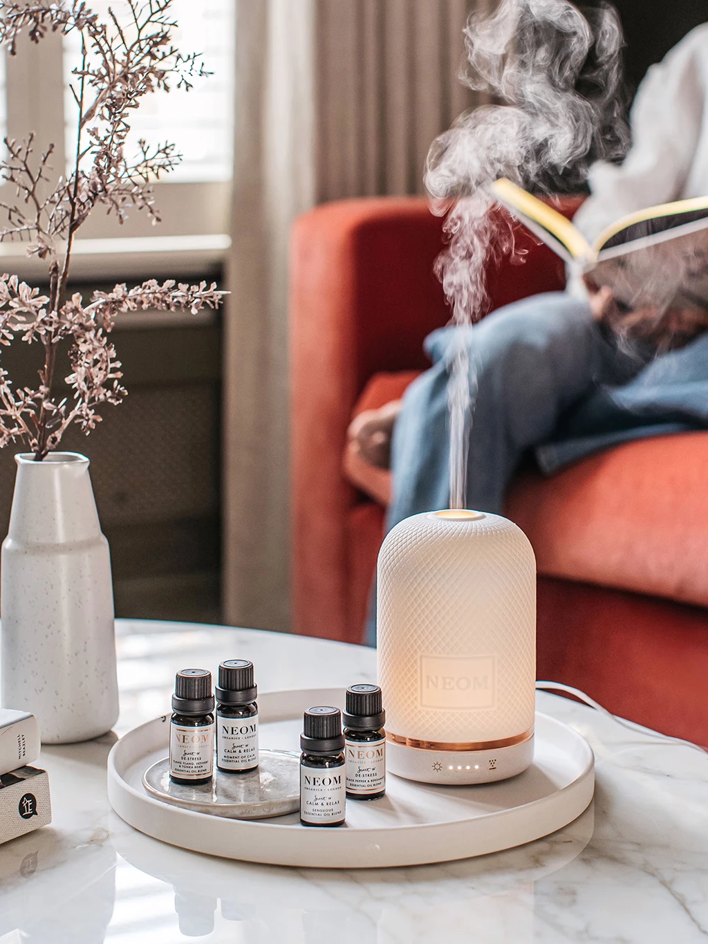 Coffee table with assorted essential oils on a tray and a Neom electronic diffuser