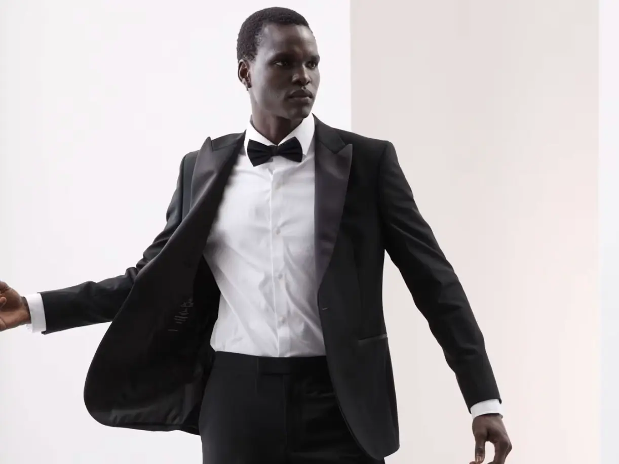 Man wearing black blazer, white shirt, smart black trousers and a black bow tie